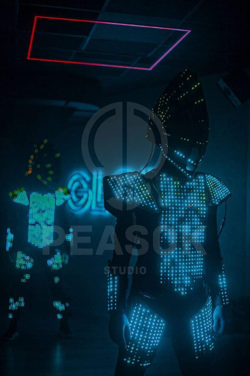 Two full-body LED pixel suits glowing in a dark studio